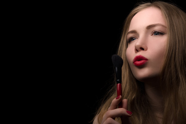 一个美丽的金发女郎肖像谁使用化妆刷在黑色的背景。图片下载