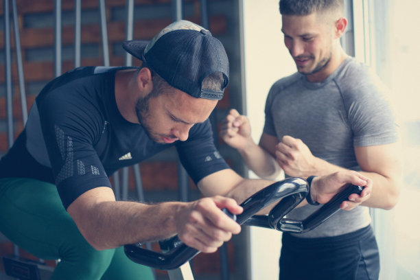 在健身课上，年轻人在固定自行车上锻炼。男人在健身房锻炼，在椭圆机上锻炼。男人的私人教练。图片下载