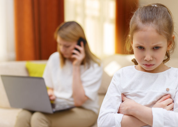 悲伤的年轻女孩。无聊的女儿和母亲在沙发上玩手机的照片。图片下载