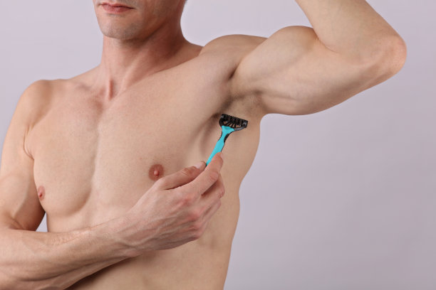 男性身体脱毛。迷人的肌肉男子用剃刀去除腋下的毛发图片下载
