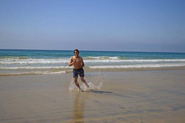 快乐的游客男子在海滩上跳高，享受在圣地亚哥，加利福尼亚，美国的假期图片下载