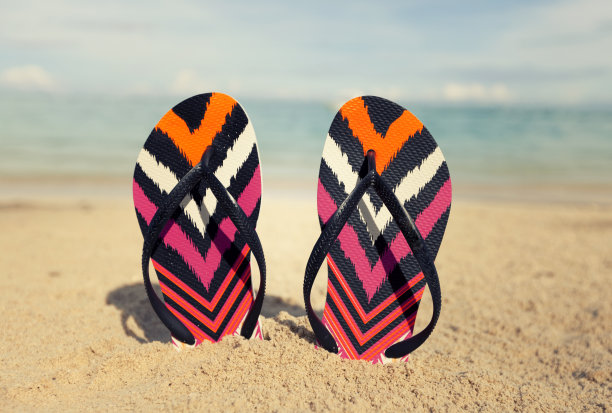 五颜六色的人字拖夹在热带海滩的沙滩上，背景是绿松石色的海洋图片下载
