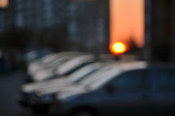 城市背景模糊。日落时的汽车和房屋。图片下载