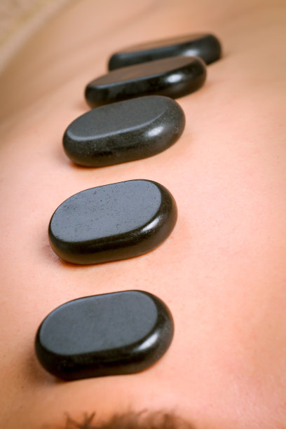 按摩治疗师按摩肩膀和背部的男性与热玄武岩石头图片下载