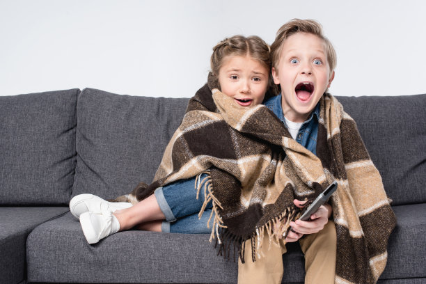 吓得弟弟和妹妹在毯子里一起看电视，孤立在白上图片下载