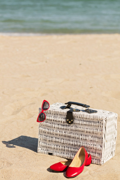 暑假在海上。白色柳条旅行箱，女士的配饰和鞋子在海滩上。图片下载