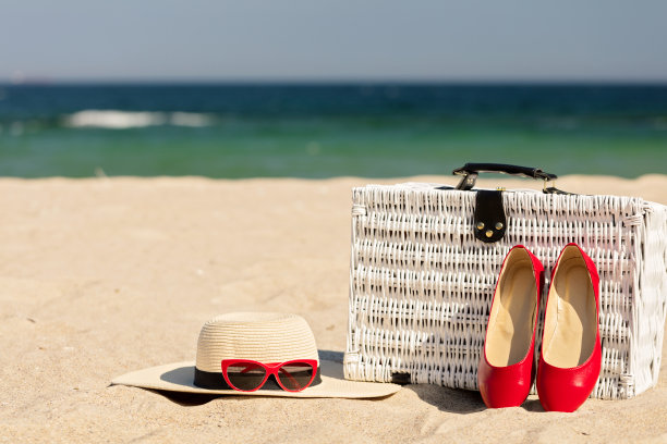 暑假在海上。白色柳条旅行箱，女士的配饰和鞋子在海滩上。图片下载