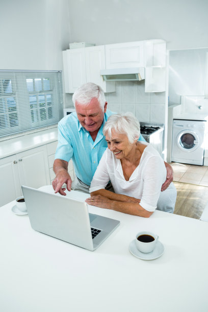 一对快乐的老年夫妇在餐桌上使用笔记本电脑图片下载
