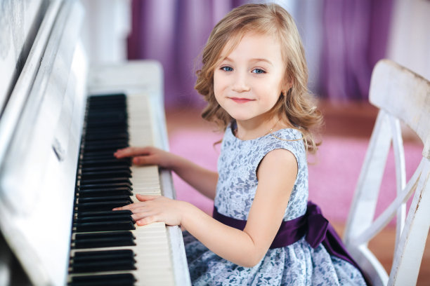 穿着漂亮裙子的金发小女孩在白色钢琴上弹奏，特写图片下载