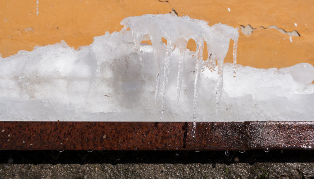 在旧墙上锈迹斑斑的金属壁架上，融化的雪和形状异常的冰柱。图片下载