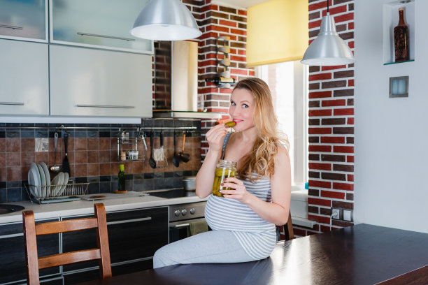 厨房里微笑的孕妇正在吃泡菜。图片下载
