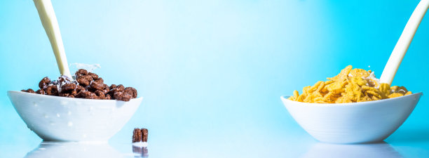 牛奶流进一个有黄色和巧克力味的碗сornflakes，牛奶溅落在杯子上，蓝色背景上有薄片。大大的照片尺寸。充满活力的明亮的颜色。图片下载