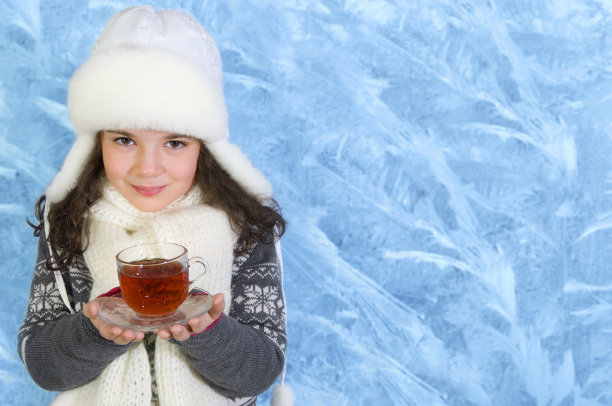 小女孩端着玻璃杯在冬天的背景上喝茶图片下载