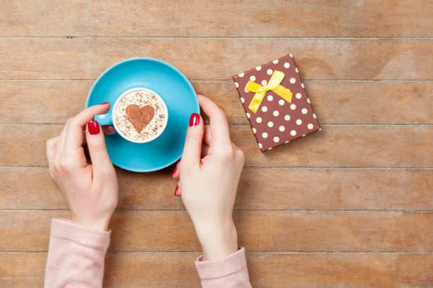 照片中的女性手捧咖啡杯附近的礼物上美妙的棕色木制背景图片下载