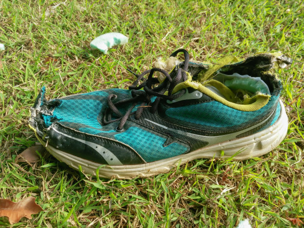 旧运动鞋在草地上损坏了。图片下载