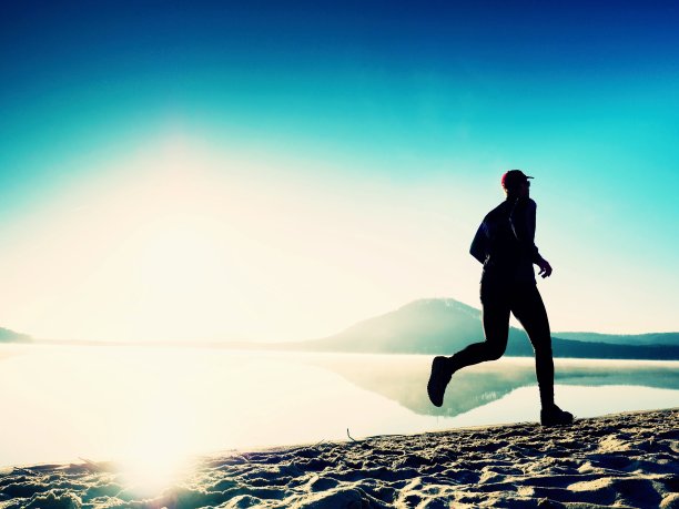 健康的生活方式。高大的跑步者正在日出的海边跑步。人在沙中跳跃图片下载