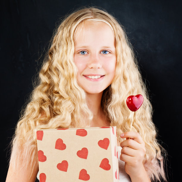 小女孩拿着礼盒和红心。可爱的少女与长金发，礼物和心图片下载