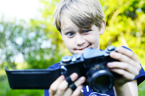 悲伤的男孩看着打开的相机背面，打开里面被毁的胶卷。一个金发小男孩拿着一台旧相机在室外拍摄。用复古胶片相机拍照的孩子。图片下载