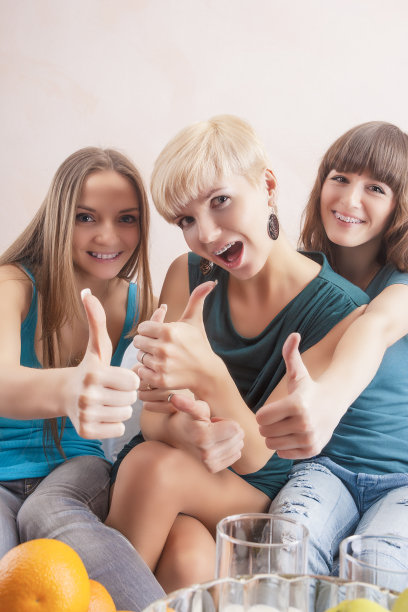 三个快乐的微笑女孩的牙齿设备显示拇指图片下载