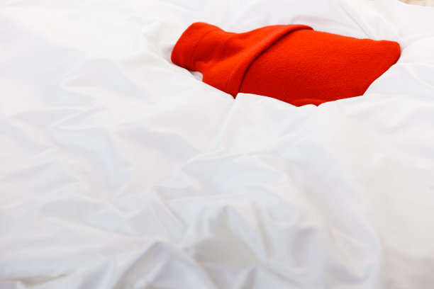 白色的被褥上放着红色的热水瓶图片下载