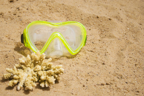 游泳面具和沙滩上的一块黄色珊瑚。运动和跳水概念图片下载