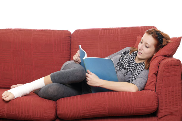 带着脚踝绷带的年轻女子在Sofà上阅读图片下载