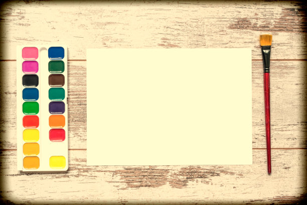 用刷子和一张白纸涂上彩色颜料，水粉，水彩画在一个古老的木制背景上，有裂缝的木制磨损板。前视图。复古复古风格的老照片。图片下载