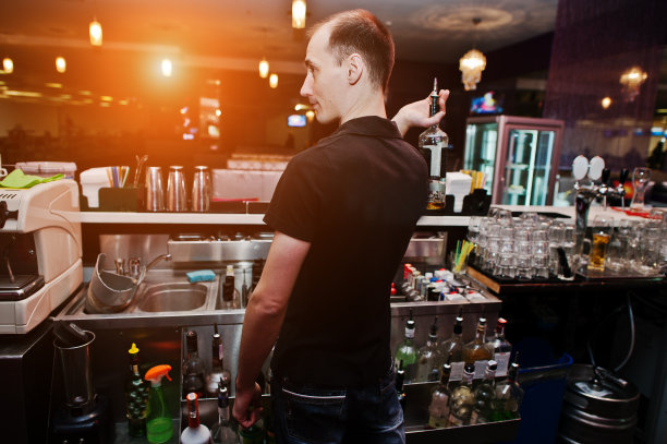 酒吧里拿着酒瓶喝鸡尾酒的年轻酒保图片下载