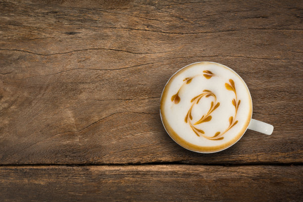 一杯拿铁咖啡俯视图。拉花艺术，心形焦糖在旧木头背景上。图片下载