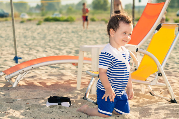 蹒跚学步的孩子穿着水手的衣服，跪在沙滩上图片下载
