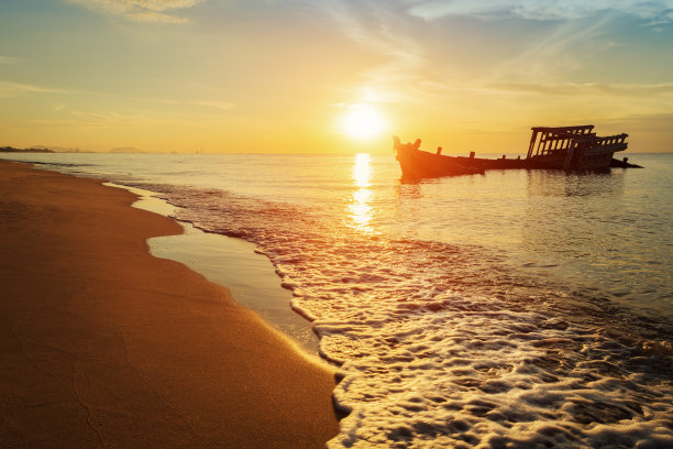 黄昏时分，海滩上一艘废弃的木制渔船的残骸图片下载