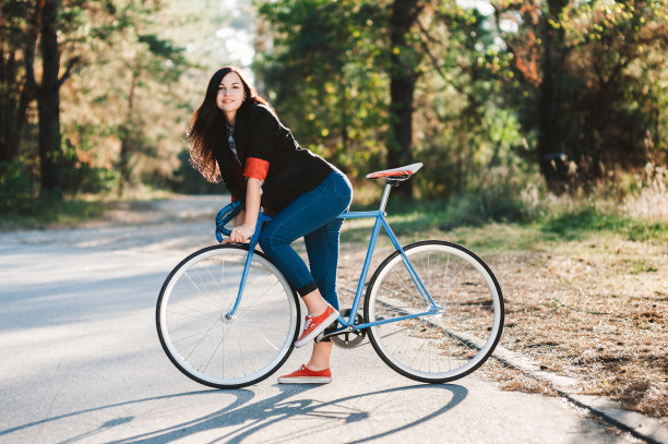 年轻的女孩潮人与固定的自行车公园在日落的背景图片下载
