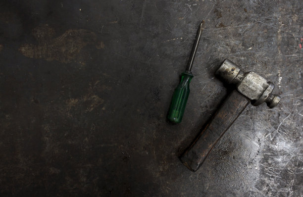 锤子和绿色螺丝刀放在有油渍的旧金属地板上。背景光线过亮，对比度过高图片下载