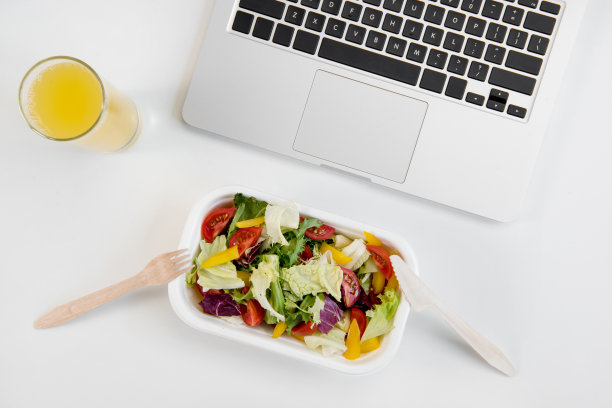 俯视图的笔记本电脑，橙汁在玻璃和新鲜沙拉在午餐盒与塑料器具在工作场所图片下载