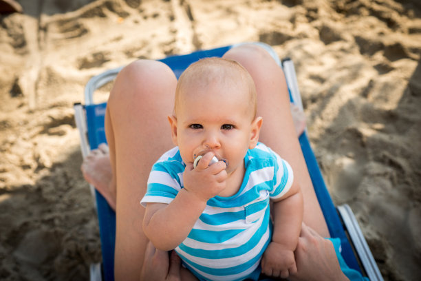 在海滩上，宝宝坐在妈妈的膝盖上图片下载