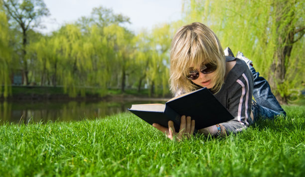 金发女孩躺在草地上看书图片下载