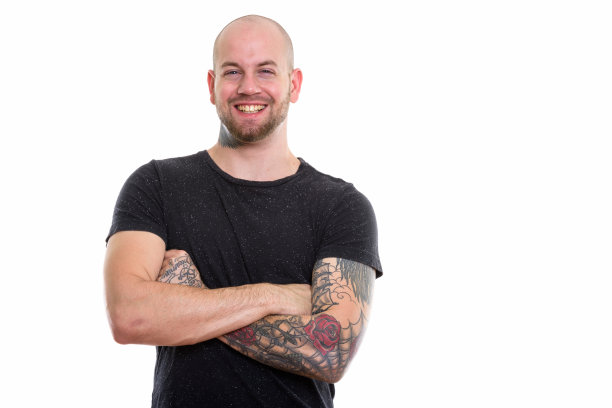 工作室拍摄的年轻快乐的秃头肌肉男微笑着双臂交叉素材图片