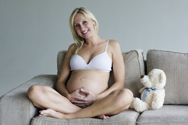 一名年轻孕妇正躺在沙发上，手里拿着一只泰迪熊图片下载
