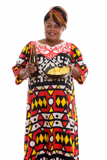 一名超重的非洲黑人妇女微笑着站在那里，手里拿着一瓶啤酒和一碗薯片图片下载