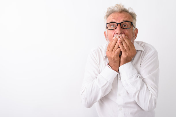 在白色背景下，一名长着胡须的帅气老男子双手捂着嘴，戴着眼镜，看起来很震惊图片下载