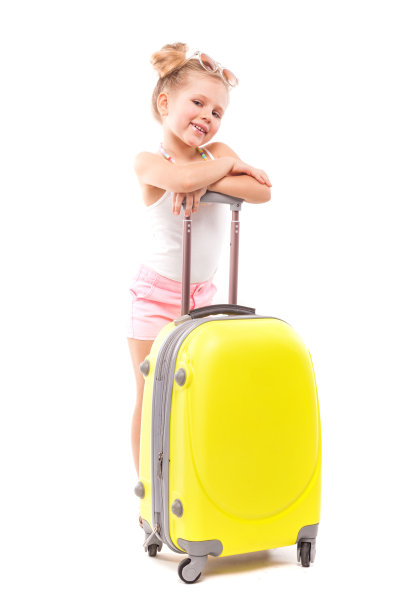 一个可爱的年轻女孩穿着白色的衬衫，粉红色的短裤和太阳镜站在黄色的手提箱旁边图片下载