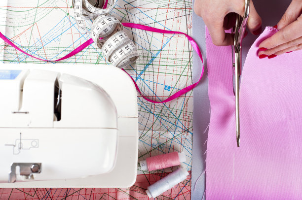 时装设计师的概念。女人的手切割粉红色的织物在工作室。模式的背景图片下载