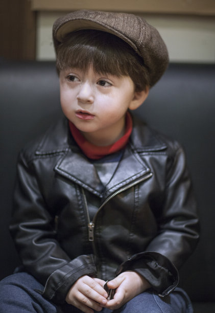 小男孩穿着黑色的乡村风格的摩托车皮夹克，戴着棕色的报童帽图片下载