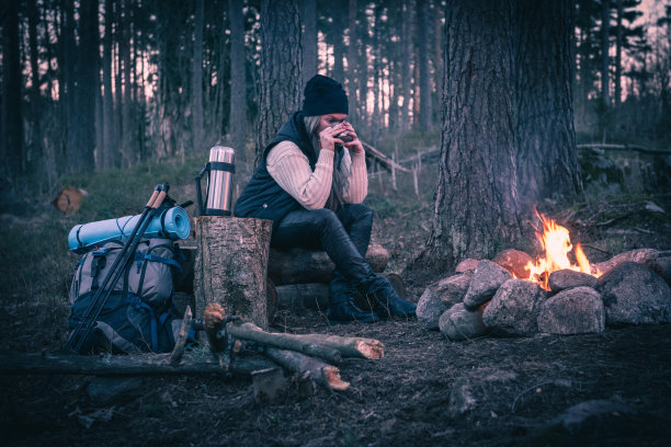 一个女人在篝火旁休息，喝着热饮图片下载