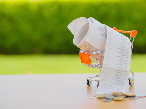 木桌上放着带有硬币收据的购物车，食品杂货支出的概念和消费主义素材图片