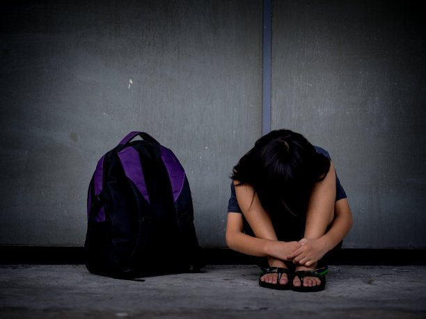 带有纹理的复古图片。悲伤的孩子坐在地板上，拿着书包等着父母。图片下载