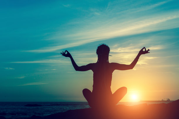 瑜伽的剪影。在令人惊叹的日落中，海上的冥想女人。图片下载