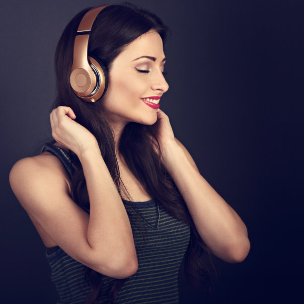 美丽冷静的年轻女子听着音乐在无线耳机与闭上眼睛在深灰色的背景。特写镜头的肖像图片下载