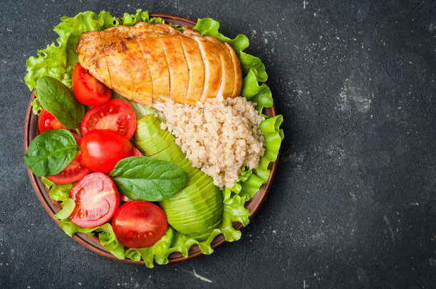 佛碗。健康晚餐有藜麦，鸡肉，西红柿，鳄梨，菠菜和莴苣叶。深色背景上的健康沙拉碗素材图片