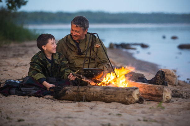 父亲和儿子在湖边的火堆旁休息。图片下载